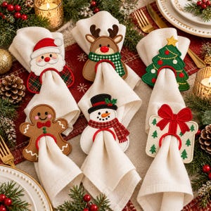 May include: A set of six embroidered felt napkin rings featuring festive holiday designs including a Santa Claus, a reindeer with a green plaid scarf, a Christmas tree, a gingerbread person, a snowman with a top hat, and a gift box with a red bow.