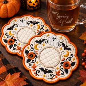May include: Two round, scalloped-edge fabric coasters featuring embroidered Halloween motifs including white ghosts, black bats, yellow crescent moons, orange flowers, and black swirls. The centre of each coaster has a quilted circular pattern.