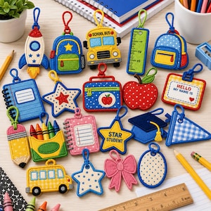 May include: A collection of colorful embroidered felt keychains featuring school-themed designs including a rocket, backpack, school bus, ruler, apple, name tag, crayons, notebook, star student badge, graduation cap, and a pink bow.