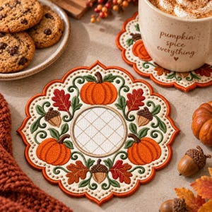 Peut inclure: Un dessous de verre rond à bords festonnés orné de motifs automnaux brodés, incluant des citrouilles orange, des glands marron et des feuilles rouges et vertes entourant un motif central en grille matelassée sur fond crème.