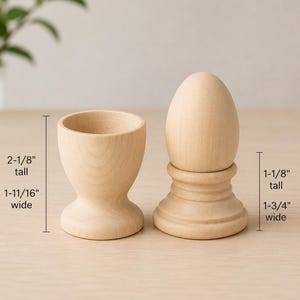 May include: A light-colored wooden egg cup and a wooden egg on a stand. The egg cup is 2-1/8 inches tall and 1-11/16 inches wide. The egg on the stand is 1-1/8 inches tall and 1-3/4 inches wide. Both items have a smooth, natural wood finish.