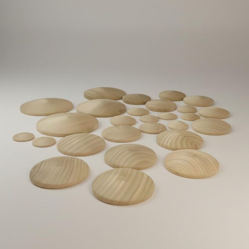 May include: A collection of numerous circular wooden discs of varying sizes, each featuring a smooth, domed top surface and a visible natural light wood grain pattern. The pieces are arranged in a scattered cluster on a plain surface.