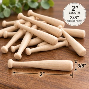 May include: A pile of small, light-coloured wooden baseball bats. Each bat measures 5.08 cm in length and 0.95 cm at the widest point, as indicated by the text and measurement lines visible in the image. The bats have a smooth, natural finish.