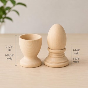 May include: A light-colored wooden egg cup and a wooden egg on a stand. The egg cup is 2-1/8 inches tall and 1-11/16 inches wide. The egg on the stand is 1-1/8 inches tall and 1-3/4 inches wide. Both items have a smooth, natural wood grain finish.