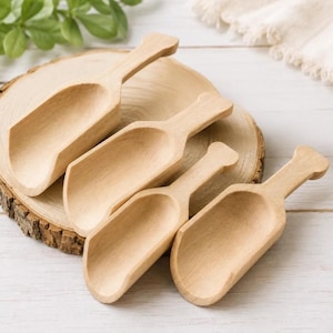 May include: A set of four light-colored wooden scoops of varying sizes, each featuring a smooth, rounded handle and a deep, concave bowl. The scoops are arranged in a cluster, showcasing the natural grain and texture of the light wood material.