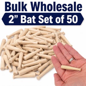 Könnte beinhalten: Ein Großhandelsset aus 50 hellen Holz-Baseballschlägern, die jeweils 5,08 cm lang sind. Das Bild zeigt einen großen Haufen dieser kleinen Schläger neben einem einzelnen Schläger in einer Handfläche zum Größenvergleich, mit dem Text Bulk Wholesale 2" Bat Set of 50.