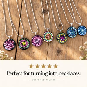 May include: Seven silver-toned chain necklaces featuring circular pendants decorated with colorful, hand-painted dot mandala patterns in various hues including pink, yellow, green, purple, and blue, arranged in a row on a wooden surface.