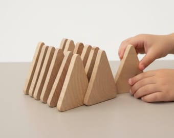 Könnte beinhalten: Ein Set aus hellen Holzblöcken in Dreiecksform, die in einer Reihe angeordnet sind. Die Blöcke haben eine glatte Oberfläche mit natürlicher Maserung und stehen aufrecht. Jedes Teil ist in Größe und Form einheitlich und bildet Spitzen.