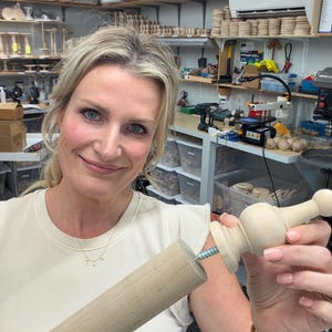 May include: A light-colored wooden dowel rod and a matching wooden finial piece with a metal screw protruding from the base, designed to be attached to the end of the rod. The components are unfinished, smooth, and light beige in color.