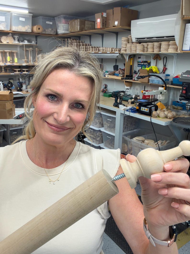 May include: A light-colored wooden dowel rod and a matching wooden finial piece with a metal screw protruding from the base, designed to be attached to the end of the rod. The components are unfinished, smooth, and light beige in color.