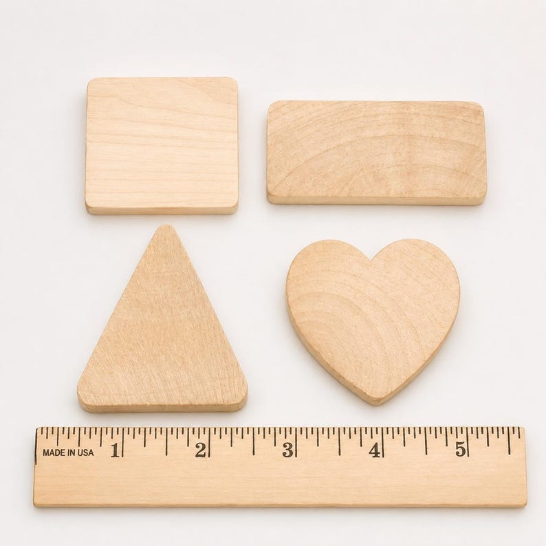 May include: Four light-colored wooden shapes including a square, a rectangle, a triangle, and a heart, arranged above a wooden ruler that measures up to 5 inches, showing the square is approximately 2 inches wide and the heart is 2 inches wide.