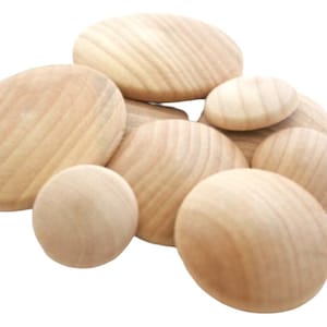 May include: A collection of smooth, unfinished wooden discs of varying sizes. Each piece features a natural light tan color with visible wood grain patterns. The circular objects are arranged in a cluster, showcasing their rounded, convex surfaces.