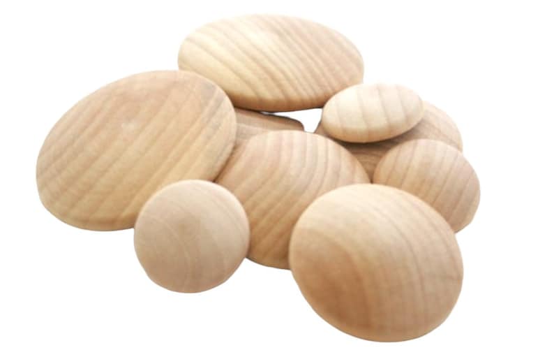 May include: A collection of smooth, unfinished wooden discs of varying sizes. Each piece features a natural light tan color with visible wood grain patterns. The circular objects are arranged in a cluster, showcasing their rounded, convex surfaces.