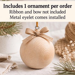 May include: A round, light-colored wooden ornament featuring a metal eyelet at the top and a tied burlap bow. The text above reads: Includes 1 ornament per order, Ribbon and bow not included, Metal eyelet comes installed.