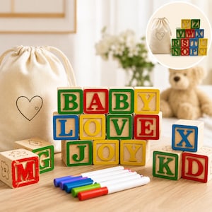 May include: Wooden alphabet blocks spelling "BABY LOVE JOY" with green, red, and yellow letters. A canvas bag with a heart design and a set of colorful markers are also present. A teddy bear is in the background.