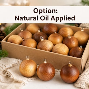May include: A collection of spherical wooden ornaments with a natural oil finish, featuring visible wood grain patterns and silver-toned metal hanging loops. The ornaments are presented in a rectangular cardboard box with text reading Option: Natural Oil Applied.
