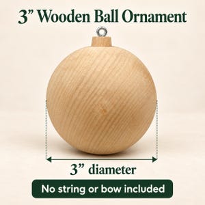 May include: A 3-inch diameter wooden ball ornament with a natural light wood grain finish and a silver-colored metal eyelet at the top. The text 3" Wooden Ball Ornament, 3" diameter, and No string or bow included is visible.