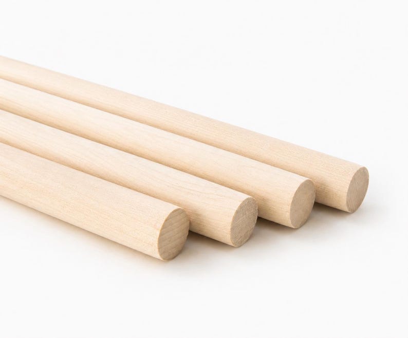 May include: Three cylindrical wooden dowels with a smooth, light beige finish. Each dowel features a uniform, straight shape with circular ends, showcasing the natural grain and texture of the light-colored wood in a simple, parallel arrangement.