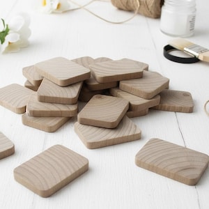May include: A collection of small, rectangular wooden tiles with rounded corners, featuring a natural light brown wood grain pattern. The tiles are arranged in a loose, overlapping pile, showcasing the smooth texture and consistent shape of each piece.