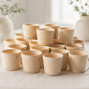 May include: A collection of small, light-colored wooden buckets, each featuring a smooth, unfinished surface and a thin, flexible metal wire handle attached to the sides. The buckets are arranged in a cluster, showing their open tops and cylindrical shapes.