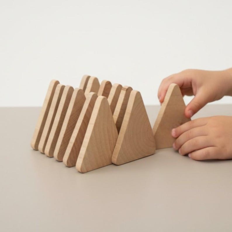 May include: A set of light-colored wooden blocks shaped like triangles, arranged in a row. The blocks have a smooth, natural grain finish and are positioned upright. Each piece is uniform in size and shape, creating a series of peaks.