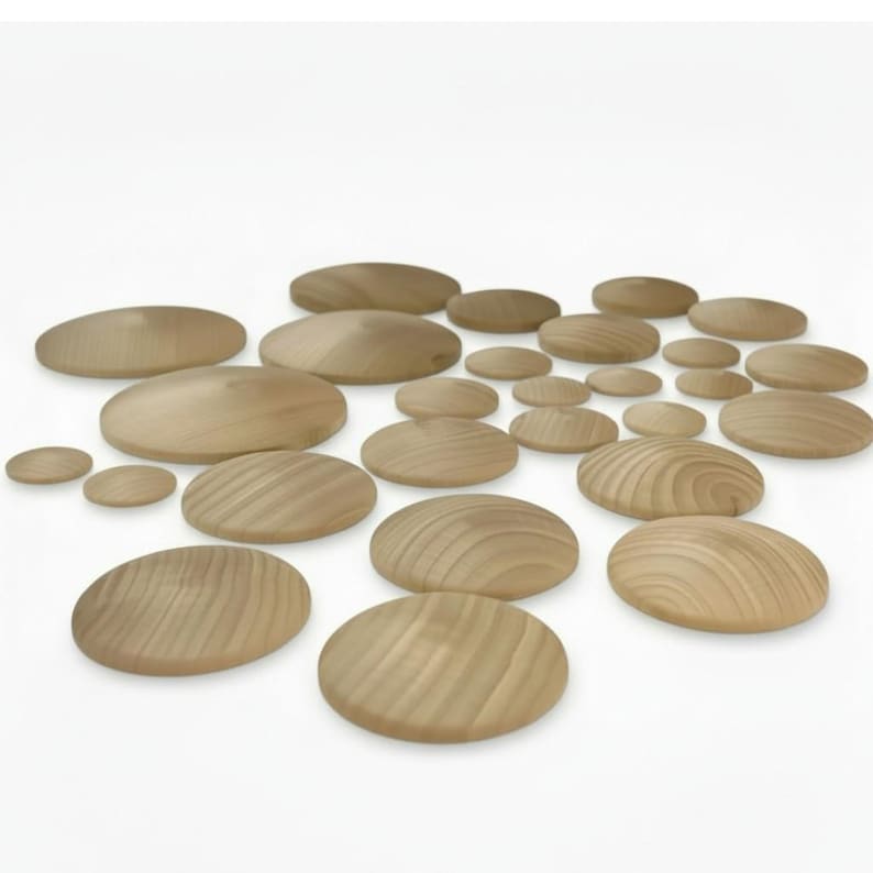 May include: A collection of numerous circular wooden discs of varying sizes, each featuring a smooth, rounded surface and a visible natural wood grain pattern in light tan tones, arranged in a scattered formation on a plain white background.