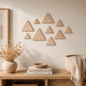 May include: A collection of ten light-colored wooden triangles arranged in a cluster on a wall. The triangles vary in size and are mounted in a scattered formation. The wood has a smooth, natural grain finish with clean, sharp edges.