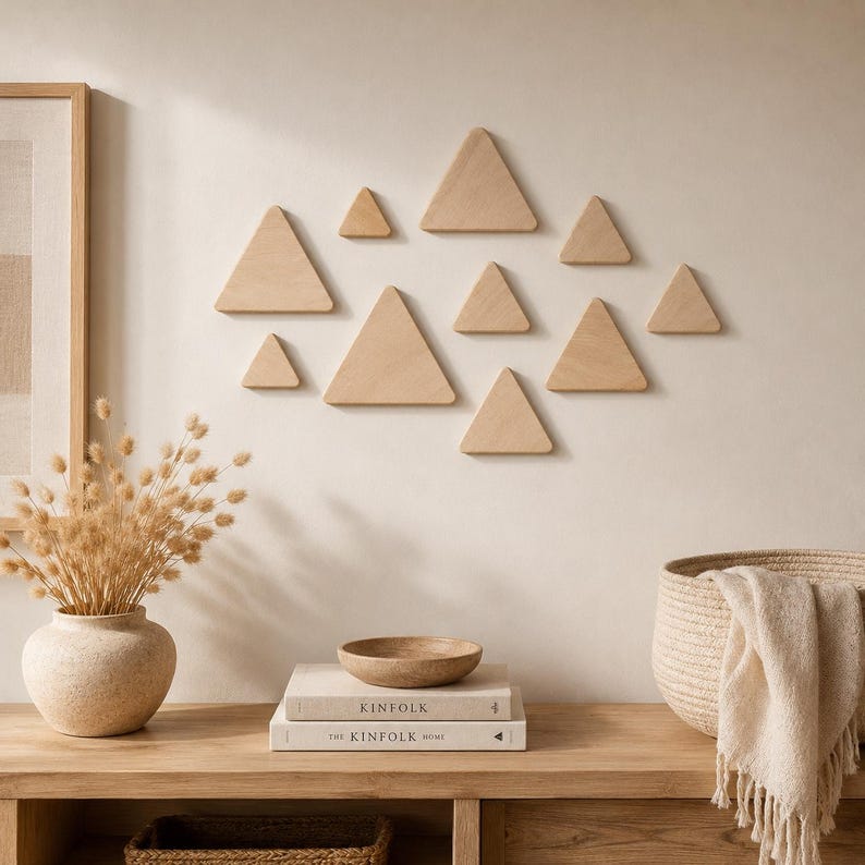 May include: A collection of ten light-colored wooden triangles arranged in a cluster on a wall. The triangles vary in size and are mounted in a scattered formation. The wood has a smooth, natural grain finish with clean, sharp edges.