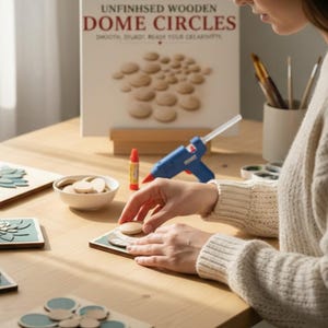 May include: A set of unfinished wooden dome circles for crafting, featuring a white display board with the text UNFINHSED WOODEN DOME CIRCLES, a blue glue gun, a small bowl of wooden circles, and square tiles with teal floral patterns.