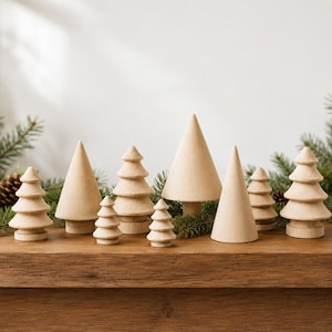 May include: A collection of nine light-coloured wooden tree figurines in various shapes and sizes, including smooth conical forms and tiered designs with horizontal ridges, arranged together on a flat wooden surface with pine branches.