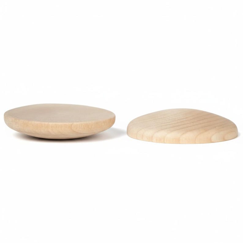 May include: Two circular wooden objects with a light beige color and visible natural wood grain. One object is positioned with its flat side facing upward, while the other is placed with its rounded, convex side facing upward on a white background.