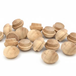 May include: A collection of unfinished wooden plugs, each with a rounded top and a slightly wider base. The plugs are light brown in color and appear to be made of natural wood. They are scattered against a white background.