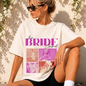 Könnte beinhalten: Ein cremefarbenes T-Shirt mit kurzen Ärmeln, das den Text "the BRIDE" in großen violetten Buchstaben und "Emma" in Schreibschrift zeigt. Unter dem Text befinden sich vier rechteckige Fotorahmen mit verschiedenen Bildern einer Person.
