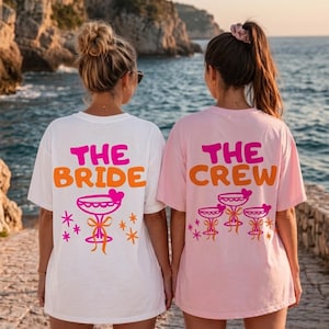 Könnte beinhalten: Ein weißes T-Shirt mit dem Text THE BRIDE in Pink und Orange über einer pinken Cocktailglas-Grafik und ein hellpinkes T-Shirt mit dem Text THE CREW in Pink und Orange über drei pinken Cocktailglas-Grafiken mit orangen Schleifen.