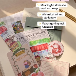 Puede incluir: Una colección de artículos de papelería que incluye un periódico titulado The Tiny Plot, una tarjeta de septiembre, una tarjeta de receta de Apple Crumble, una pegatina de caracol, una pegatina de manzana y un marcapáginas sobre un cuaderno.