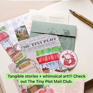 May include: A collection of stationery items including a newspaper titled The Tiny Plot, a green envelope, a gold fountain pen, various illustrated cards, and stickers featuring a snail and an apple, all arranged on a large open notebook.