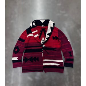 Puede incluir: Un cárdigan estampado en rojo, negro y blanco, con cuello chal. El suéter presenta diseños geométricos y rayas horizontales. Tiene cierre de botón y un cordón. La paleta de colores incluye tonos de rojo, negro y blanco.