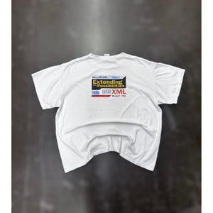 May include: White t-shirt with a graphic on the back that reads "Extending the Possibilities" with the Microsoft .NET logo and the words SOAP and XML. The shirt is laid flat on a dark surface.
