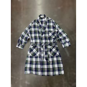 Puede incluir: Bata a cuadros en azul, verde y blanco. La bata tiene cuello chal, mangas largas, dos bolsillos delanteros y un cinturón a juego. La bata está hecha de una tela suave y tejida y está colocada sobre una superficie neutra.