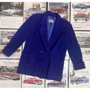 Puede incluir: Un blazer azul real vibrante con frente de doble botonadura con dos botones visibles, solapas de muesca, mangas largas con puños doblados y dos grandes bolsillos de parche en la parte delantera. El interior está forrado con tela azul a juego.