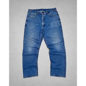 Puede incluir: Un par de pantalones vaqueros de mezclilla azul con lavado medio que presentan un diseño clásico de cinco bolsillos, cierre de botones, trabillas para cinturón en la cintura y costuras en contraste de color naranja a lo largo de las costuras.