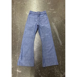 May include: Light blue denim pants featuring a high-waisted design with a button and zipper fly closure. These trousers include two large patch pockets on the front and a wide-leg silhouette that flares slightly toward the bottom hemline.