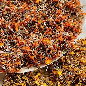 May include: A large collection of dried orange marigold petals mixed with thin, dark brown and white seed husks. A small square logo in the bottom right corner features a key icon and the text Forest Key, with smaller text below it.
