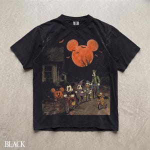 May include: A black short-sleeve t-shirt featuring a graphic print of Disney characters riding bicycles at night. The scene includes a large orange moon shaped like Mickey Mouse, a house, a pumpkin, and bats against a dark, spooky background.