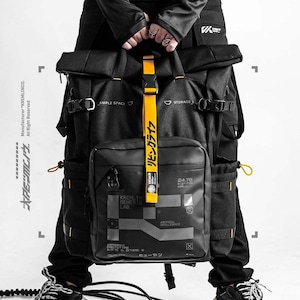 Peut inclure: Un sac à dos tactique noir doté d'une fermeture à enroulement, de multiples boucles latérales et d'une sangle verticale jaune avec du texte japonais. La poche avant présente des graphismes blancs imprimés dont le texte KREMLIN GENESIS LAB.