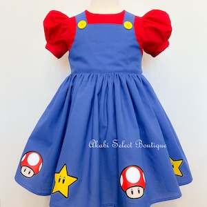 May include: A blue and red dress with a puff sleeve and a red bodice. The dress has a star and mushroom design on the skirt. The text "Akabi Select Boutique" is printed on the skirt.