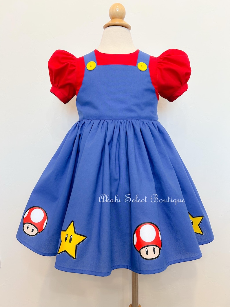 May include: A blue and red dress with a puff sleeve and a red bodice. The dress has a star and mushroom design on the skirt. The text "Akabi Select Boutique" is printed on the skirt.