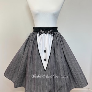 May include: A black and white striped skirt with a white panel and black buttons. The skirt has a black bow at the waist and the text "Akabi Select Boutique".