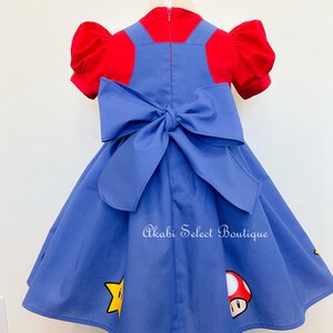 May include: A blue dress with a red top and a large bow in the back. The dress has a star and mushroom design. The text "Akabi Select Boutique" is printed on the dress.