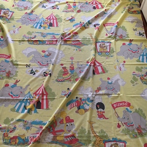 May include: Yellow fabric with a repeating pattern of a circus scene featuring Dumbo the elephant, a train, a giraffe, and a lion in a cage. The fabric has a vintage look and feel.